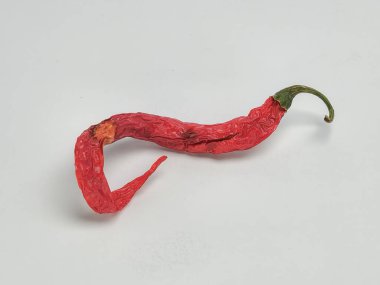 Sade beyaz bir arka planda izole edilmiş tek bir kırmızı biberli yakın çekim stüdyo fotoğrafı. Biber buruşuk ve kıvrımlı, kuruma belirtileri gösteriyor. Sapı yeşil ve toplam rengi koyu kırmızı renktedir. Bu resim mutfak için uygundur.