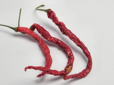 Yakın çekim stüdyo çekimlerinde beyaz arka planda üç adet kurutulmuş kırmızı biber vardı. Biberler buruşuk ve canlı renkteler. Dokularını ve şekillerini sergiliyorlar. Görüntü, doğal şekilleri vurgular..