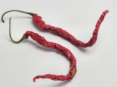 Temiz beyaz arka planda iki kurutulmuş kırmızı biber sergilenir. Biberlerin buruşuk bir dokusu ve canlı kırmızı bir rengi var. Baharatlı bir tadı var. Görüntü iyi aydınlatılmış ve biberlerin şekli ve dokusuna odaklanmış..