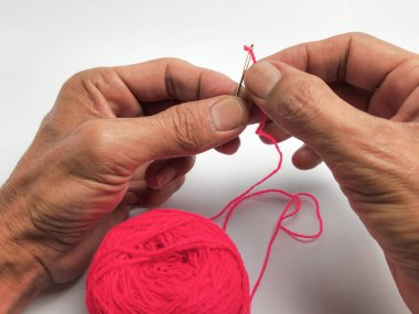 Yakından çekilen bir fotoğraf, parlak pembe iplikle iğne ipliği tutan birinin ellerini yakalar. Görüntü, dikişin titiz sürecini vurguluyor. Parmaklar arasında tutulan iğne ve göz boyunca dikkatlice yönlendirilen iplik..