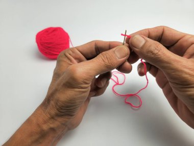 Yakından çekilen bir fotoğraf, parlak pembe iplikle bir iğneyi dikkatlice iplikçikleyerek bir insanın ellerini yakalar. Aynı iplikten oluşan bir top yakınlarda duruyor ve beyaz arka planda basit bir kompozisyon oluşturuyor. Resim dikiş dikmenin odaklanmış eylemini vurgular.