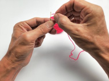 İğneye iplik geçireni gösteren yakın plan bir fotoğraf. Ellere ve şırıngaya odaklanmış, iğnenin gözüne saplanmış canlı pembe bir iplik var. Arka plan bembeyaz, elleri ve görevi vurguluyor.. 