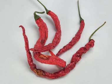 Beyaz arka planda birkaç kurutulmuş kırmızı biberin yakın plan çekimi. Biberler buruşuk ve canlı kırmızı renkteler. Bu da acı ve baharatlı olduklarını gösteriyor. Biberlerin dokusuna ve rengine odaklanan kompozisyon basittir.