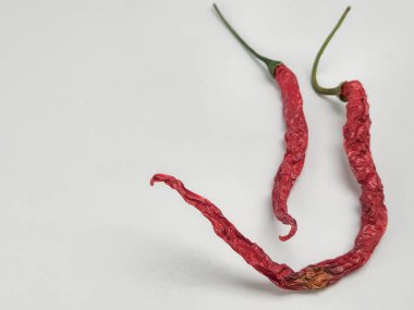 Sade beyaz arka planda iki kurutulmuş kırmızı biberin yakın plan çekimi. Biberlerin buruşuk bir dokusu ve canlı bir rengi var. Odak keskin, biberlerin detaylarını gösteriyor...