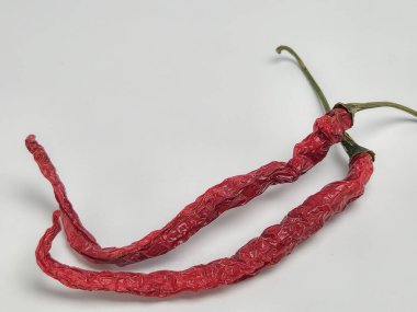 Bu resim, düz beyaz arka planda iki kurutulmuş kırmızı biber içeriyor. Biberler buruşuk ve canlı kırmızı bir renge sahip. Şekillerini ve dokularını vurgulayarak köşegen bir kompozisyonda konumlandırılmışlardır...