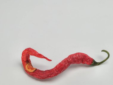 Stüdyoda tek bir kırmızı kırmızı biberin beyaz arka plana doğru kıvrılarak yakın plan çekimi. Biber buruşmuş, yaşını ve dokusunu gösteriyor. Canlı kırmızı rengi, temiz arkaplanla çok güzel zıtlaşıyor..