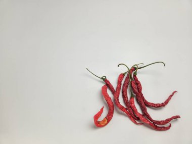 Kurutulmuş kırmızı biber kümesi düz beyaz bir arkaplanda duruyor. Biberler görsel olarak ilginç bir kompozisyonda dizilmiş, dokularını ve renklerini gösteriyorlar. Görüntü, doğal besin, sağlıklı beslenme ve baharatlı lezzeti çağrıştırıyor.