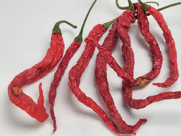 Beyaz arka planda birkaç kurutulmuş kırmızı biberin yakın plan çekimi. Biberler buruşuk ve buruşuk, kurumuş dokularını ve renklerini gösteriyor. Çekim iyi aydınlatılmış, dokuları vurguluyor..