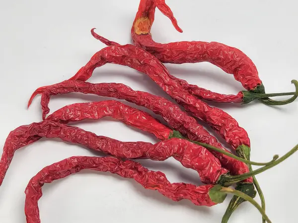 Yakın çekim, beyaz bir yüzeye yerleştirilmiş kırmızı biberleri yakalar. Biberler buruşuk dokular ve canlı kırmızı renkler sergiliyor. Bileşim, sapları ve kapakları görünür olan doğal şekilleri vurgular..