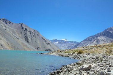 El Yeso Reservoir, And Dağları 'ndaki bir baraj boyunca saklanan yapay bir su deposudur. Nevado Piuquenes arka planda görülebilir.