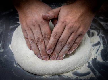 Quito, Ekvador - 14 Haziran 2025: Pizzayı şekillendiren malzemeleri karıştıran uçlu eller. Ev yapımı bir pizzayı paylaşmanın lezzetini ve neşesini öngören basit, sanatsal bir hareket..