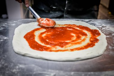 Nazikçe pizza hamuruna kaşık ile domates sosu ekleyin, aroma ve renkle karıştırın. Zengin aromalarla dolu bir pizzanın başlangıcı olan basit bir jest..