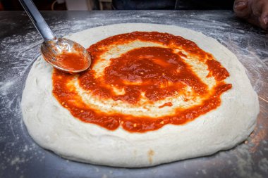 Nazikçe pizza hamuruna kaşık ile domates sosu ekleyin, aroma ve renkle karıştırın. Zengin aromalarla dolu bir pizzanın başlangıcı olan basit bir jest..