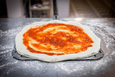 Ev yapımı domates sosuyla kaplı, pizza kabuğunun üzerinde yeni uzatılmış bir pizza tabanı..