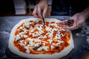 Uzman eller dikkatlice domates sosu ve peynirle kaplı bir pizza tabağına incir meyvesi parçaları serptiler..