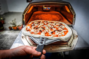 Çiğ pizzayı nazikçe fırının içine yerleştiriyor ve mükemmel pişirmeye başlıyor..