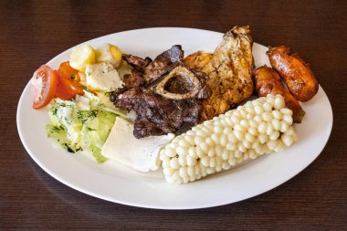 Ekvador asado 'su, yanında mısır, taze peynir, sosis ve domates salatası ile birlikte tavuk, sosis ve sığır eti karışımı beyaz bir tabakta servis edildi. Lezzetli bir And yemeği..