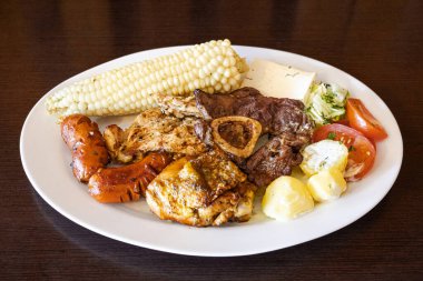 Beyaz bir tabakta servis edilen Ekvador rostosunun yanında tavuk, sosis ve sığır eti karışımı mısır, taze peynir, soslu patates ve domates salatası var. Lezzetli bir And yemeği..