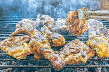 Izgara maşası kullanarak, ızgara tavuğu kızgın kömürlerin üzerinde çevirerek. Dumanın içinde leziz et parçaları ve ateş. Geleneksel bir yemek, aile toplantıları ve hafta sonları için mükemmel.. 