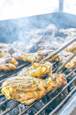 Izgara maşası kullanarak, ızgara tavuğu kızgın kömürlerin üzerinde çevirerek. Dumanın içinde leziz et parçaları ve ateş. Geleneksel bir yemek, aile toplantıları ve hafta sonları için mükemmel.. 