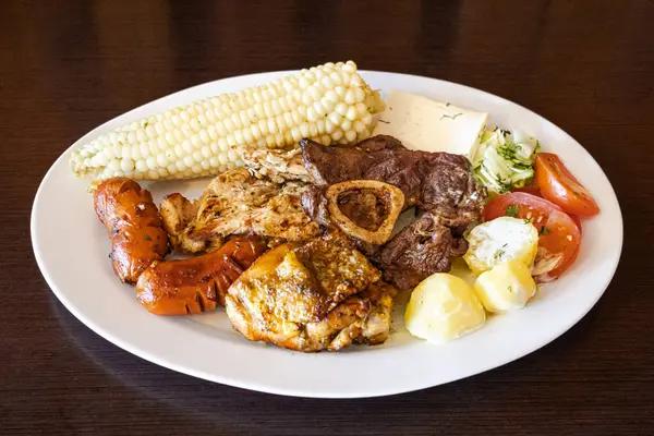 Beyaz bir tabakta servis edilen Ekvador rostosunun yanında tavuk, sosis ve sığır eti karışımı mısır, taze peynir, soslu patates ve domates salatası var. Lezzetli bir And yemeği..