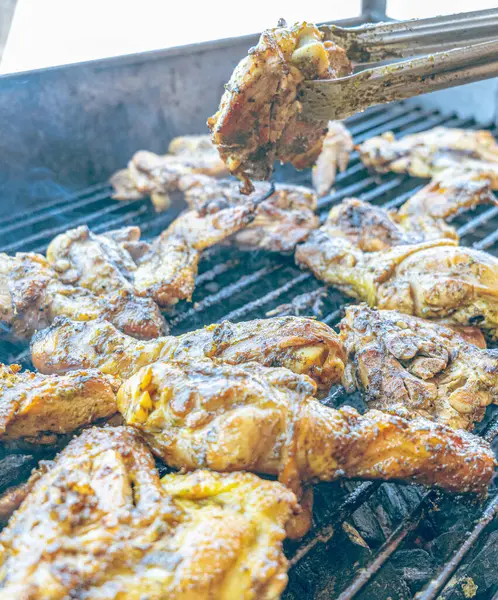 Izgara maşası kullanarak, ızgara tavuğu kızgın kömürlerin üzerinde çevirerek. Dumanın içinde leziz et parçaları ve ateş. Geleneksel bir yemek, aile toplantıları ve hafta sonları için mükemmel.. 