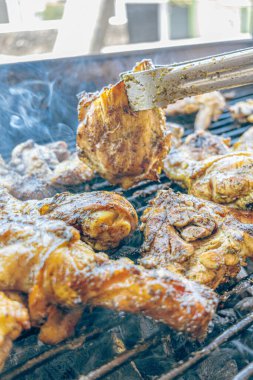 Izgara maşası kullanarak, ızgara tavuğu kızgın kömürlerin üzerinde çevirerek. Dumanın içinde leziz et parçaları ve ateş. Geleneksel bir yemek, aile toplantıları ve hafta sonları için mükemmel.. 