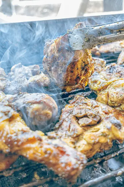 Izgara maşası kullanarak, ızgara tavuğu kızgın kömürlerin üzerinde çevirerek. Dumanın içinde leziz et parçaları ve ateş. Geleneksel bir yemek, aile toplantıları ve hafta sonları için mükemmel.. 