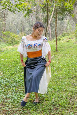 Doğayla uyum içinde dans eden Otavalo yerlisi kadın, anako, nakışlı bluz, altın walka kolye, kahverengi manila kemeri ve manilla ya da bilezik takıyor..