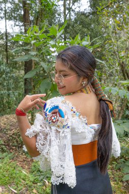 Doğayla uyum içinde Otavalo yerlisi bir kadın, anako, nakışlı bluz, altın walka kolye, renkli manila kuşağı ve manilla ya da bilezik takıyor..