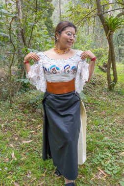 Doğayla uyum içinde Otavalo yerlisi bir kadın, anako, nakışlı bluz, altın walka kolye, renkli manila kuşağı ve manilla ya da bilezik takıyor..