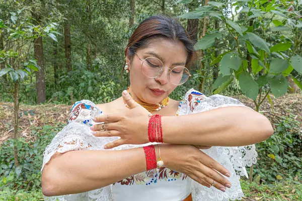 Otavalea yerlisi bir kadın kırmızı bileziğini ya da manillasını gösteriyor. Geleneksel kıyafetleri anako işlemeli bluz, altın walka kolyesi takıyor..