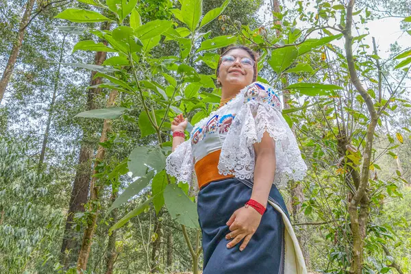 Doğayla uyum içinde Otavalo yerlisi bir kadın, anako, nakışlı bluz, altın walka kolye, renkli manila kuşağı ve manilla ya da bilezik takıyor..