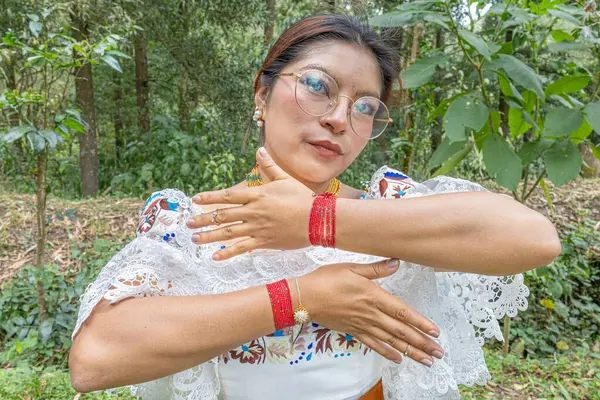 Otavalea yerlisi bir kadın kırmızı bileziğini ya da manillasını gösteriyor. Geleneksel kıyafetleri anako işlemeli bluz, altın walka kolyesi takıyor..