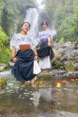 Geleneksel giyinmiş iki Otavalo yerlisi kadın, Pawkar Raymi 'de, Peguche Şelalesi' nin yanında doğa ve ruhanilikle derin bir bağ içinde tarihi bir Tumarina ayini düzenler..