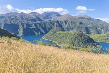 Cuicocha Lagoon in the Ecuadorian Andes, a wheat field, and in the background the majestic Cotacachi Volcano with its summit hidden among the clouds. An Andean landscape of great natural beauty.