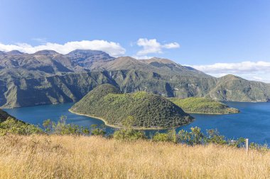 Cuicocha Lagoon in the Ecuadorian Andes, a wheat field, and in the background the majestic Cotacachi Volcano with its summit hidden among the clouds. An Andean landscape of great natural beauty.