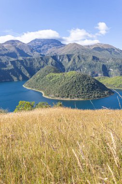 Cuicocha Lagoon in the Ecuadorian Andes, a wheat field, and in the background the majestic Cotacachi Volcano with its summit hidden among the clouds. An Andean landscape of great natural beauty.