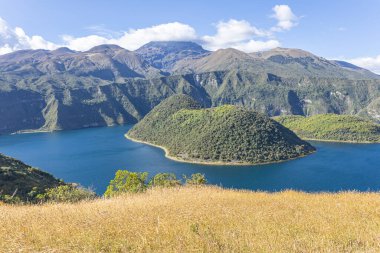 Cuicocha Lagoon in the Ecuadorian Andes, a wheat field, and in the background the majestic Cotacachi Volcano with its summit hidden among the clouds. An Andean landscape of great natural beauty.