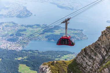 Pilatus Dağı 'nın tepesine çıkan parlak kırmızı bir teleferiğin çarpıcı görüntüsü. Aşağıda Lucerne Gölü ve İsviçre Alpleri var. Açık bir günde yakalanan bu sahne, İsviçre turizmini, dağcılık maceralarını ve açık hava eğlencelerini göstermek için mükemmel..