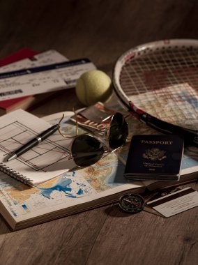 Pasaport, bavul, biniş kartı, tenis raketi, top, defter, kalem, güneş gözlüğü, pusula, atlas ve bir seyahat için kredi kartı içeren seyahat temalı bir düzenek..