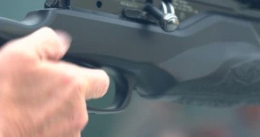 Bir el dışarıdaki atış poligonunda bir silahın üzerine yerleştirilir. Atıcının antrenmana hazırlanırken kavrama ve güvenlik mekanizmasına odaklanacağız. Çevre açık ve güneşli..