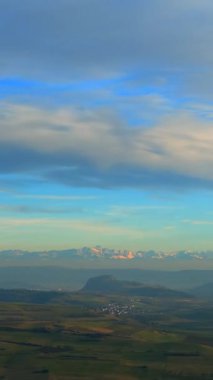Huzurlu vadilerin üzerinde görkemli dağlar yükselir, yumuşak sabah ışığında yıkanır. Sakin ortam yansımayı davet ederken doğa karanlıktan uyanır..