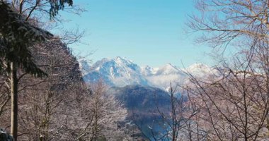 Kar görkemli dağları örtüyor, parlak mavi gökyüzünün altında çarpıcı bir manzara yaratıyor. Çam ağaçları kışın doğanın güzelliğini artırmak için manzarayı çerçeveler..