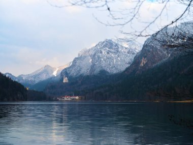Sakin bir göl bulutlu bir gökyüzünün altında karla kaplı dağları yansıtır. Huzurlu sahne, güzel bir açık havada güzel bir kış gününü yakalıyor..