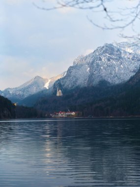Sakin sular, vadide yuva yapmış tuhaf bir köyün arkasında güneş batarken yükselen dağları yansıtıyor. Manzara, kışın bir ipucuyla doğal güzellikleri gözler önüne seriyor..