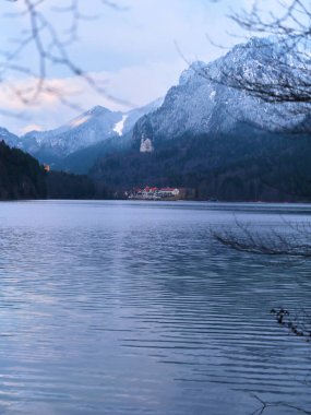 Sakin bir göl üzerinde karla kaplı dağlar yükseliyor, su yüzeyinde yansımalar parıldıyor. Karanlık çöktüğünde Bavyera 'nın cennet manzarasına bakan tarihi bir şato ağaçların arasından bakıyor..