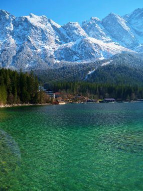 Turkuaz sular, berrak mavi gökyüzünün altındaki görkemli karlı tepeleri yansıtır. Bereketli ormanlar kıyıya sarılıyor, sakin bir manzara yaratıyor doğa severler için mükemmel..