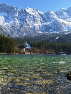 Sakin bir dağ gölü, berrak mavi gökyüzünün altında karla kaplı çarpıcı tepeleri yansıtır. Uzun çam ağaçları kıyı şeridini kuşatarak dinlenmek için mükemmel bir cennet yaratıyor..