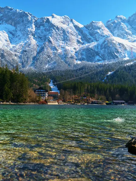 Sakin bir dağ gölü, berrak mavi gökyüzünün altında karla kaplı çarpıcı tepeleri yansıtır. Uzun çam ağaçları kıyı şeridini kuşatarak dinlenmek için mükemmel bir cennet yaratıyor..
